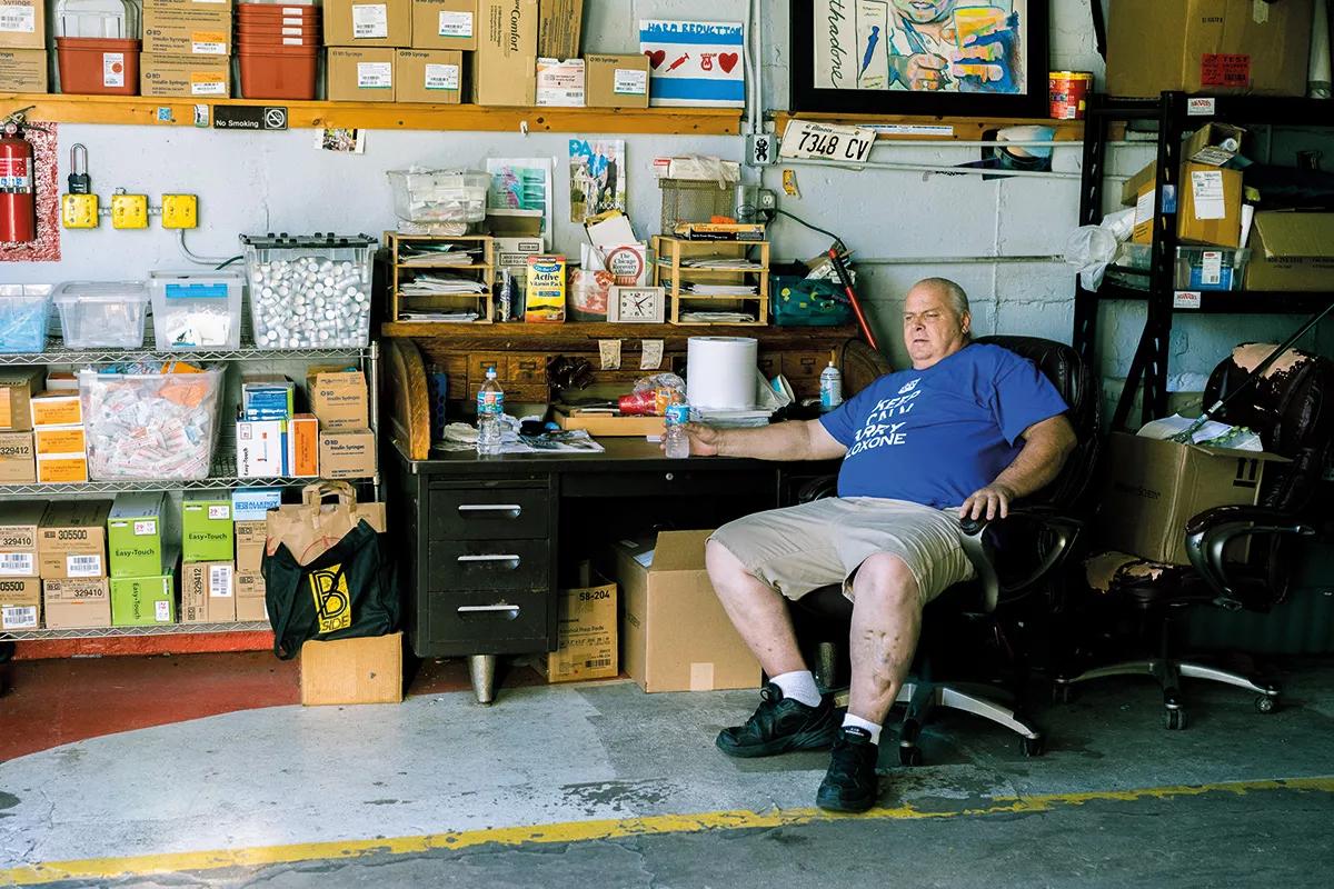 John Gunterson, sentado en el garaje en el que se guardan las camionetas de intercambio de jeringuillas de la Chicago Recovery Alliance. Gunterson, lleva puesta una camiseta con el lema “Keep calm and carry naloxone” diseñada por el propio Nigel Brunsdon.